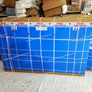 Pode incluir: Uma caixa de cart&atilde;o azul com um padr&atilde;o de grade branca e v&aacute;rias etiquetas "FRAGILE HANDLE WITH CARE". A caixa &eacute; segura com um cord&atilde;o branco.