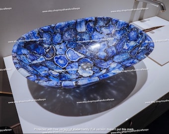 May include: An oval-shaped vessel sink constructed from polished blue agate stone slices. The basin features a mosaic pattern of deep blue, light blue, and white crystalline segments with dark veining, centered with a circular metal drain plug.