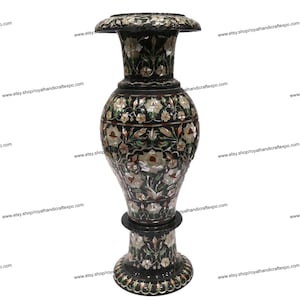 Puede incluir: Un jarrón de mármol negro con intrincados diseños florales incrustados con nácar y otras piedras de colores. El jarrón tiene una boca ancha y una base redonda.