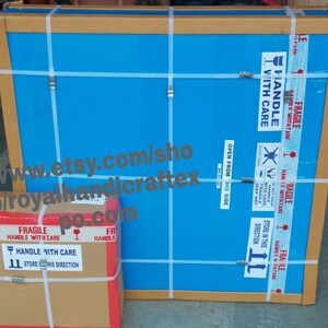 May include: Two cardboard boxes with blue and brown tape. The larger box has a blue surface with the text "HANDLE WITH CARE" and "OPEN FROM THIS SIDE". The smaller box has a brown surface with the text "FRAGILE HANDLE WITH CARE" and "STORE IN THIS DIRECTION". The text "www.etsy.com/shop/p/royalhandicraftex.po.com" is visible on the boxes.