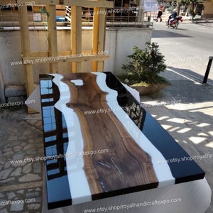 Peut inclure: Un plateau de table en résine époxy noire et blanche avec un grain de bois naturel. Le plateau de table est fait d'une épaisse dalle de bois avec une rivière de résine époxy blanche qui la traverse. Le plateau de table est fini avec une résine époxy noire brillante.
