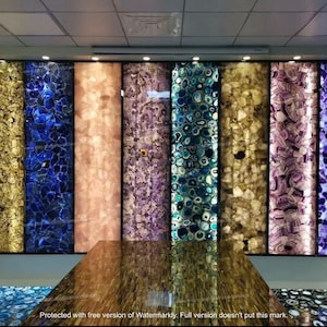 May include: A wall display of agate slabs in various colors, including blue, purple, pink, and yellow. The slabs are arranged vertically and are illuminated from behind, creating a shimmering effect.