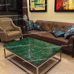 Puede incluir: Una mesa de centro de malaquita verde con un marco de metal plateado. La mesa está en un salón con un sofá de cuero marrón y una silla.