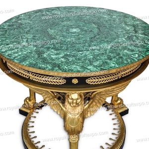 May include: A round, green marble top table with gold accents and a black base. The base features a winged lion design and a circular, gold-trimmed base.
