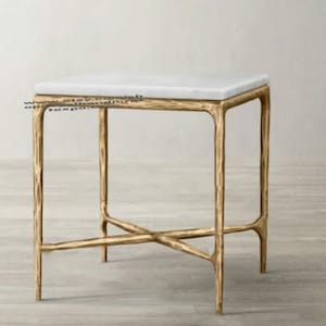 Può includere: Un tavolino da salotto in metallo dorato con un piano in marmo bianco. Il tavolino ha un design semplice e moderno con un piano quadrato e quattro gambe.