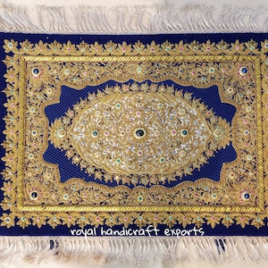 May include: A blue velvet rug with gold embroidery and jewel-toned accents. The rug has a fringed border and the text "royal handicraft exports" is embroidered in the bottom center.