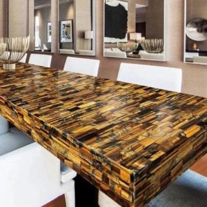 May include: A large dining table with a polished tiger's eye stone top. The table is surrounded by white chairs and has a modern design.