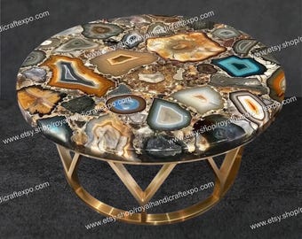May include: Oval coffee table with a mosaic agate stone top in shades of brown, gray, and blue. The table has a gold-colored metal base with a geometric design. A unique piece for any living space.
