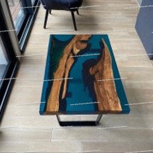 May include: A teal blue and brown epoxy resin coffee table with a black metal base. The table top has a natural wood grain pattern and a unique blue resin pour.