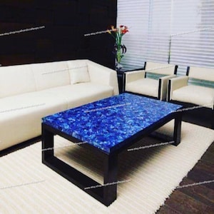 May include: A blue and black coffee table with a unique lapis lazuli inlay top. The table is surrounded by white leather furniture and a white rug.
