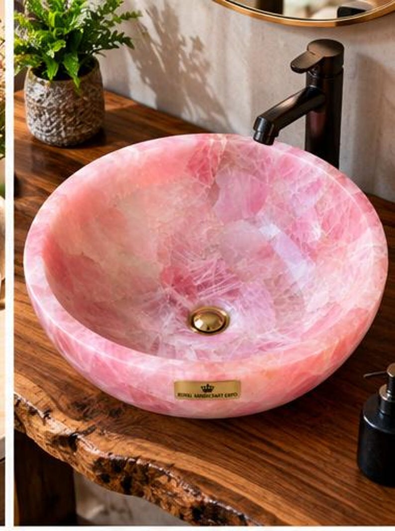 Pode incluir: Uma cuba de apoio redonda feita de pedra de quartzo rosa transl&uacute;cido com acabamento polido. A bacia apresenta um ralo em tom dourado e uma pequena placa retangular de lat&atilde;o com o texto ROYAL HANDICRAFT EXPO na borda frontal.