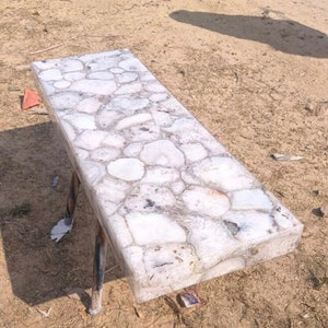 May include: White agate coffee table with a unique, natural stone top. The table has a rectangular shape and is supported by two metal legs.