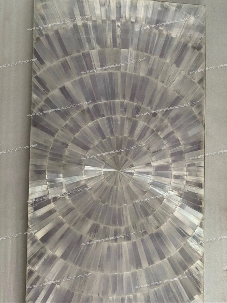 May include: A circular, gray and white mosaic tile with a radial pattern. The tile is made of many small, rectangular pieces of selenite, a type of crystal. The tile has a unique, geometric design.