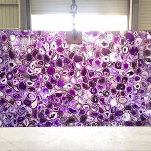 May include: A large slab of purple agate with a variety of shapes and sizes of agate slices. The agate is a natural stone with a polished finish.