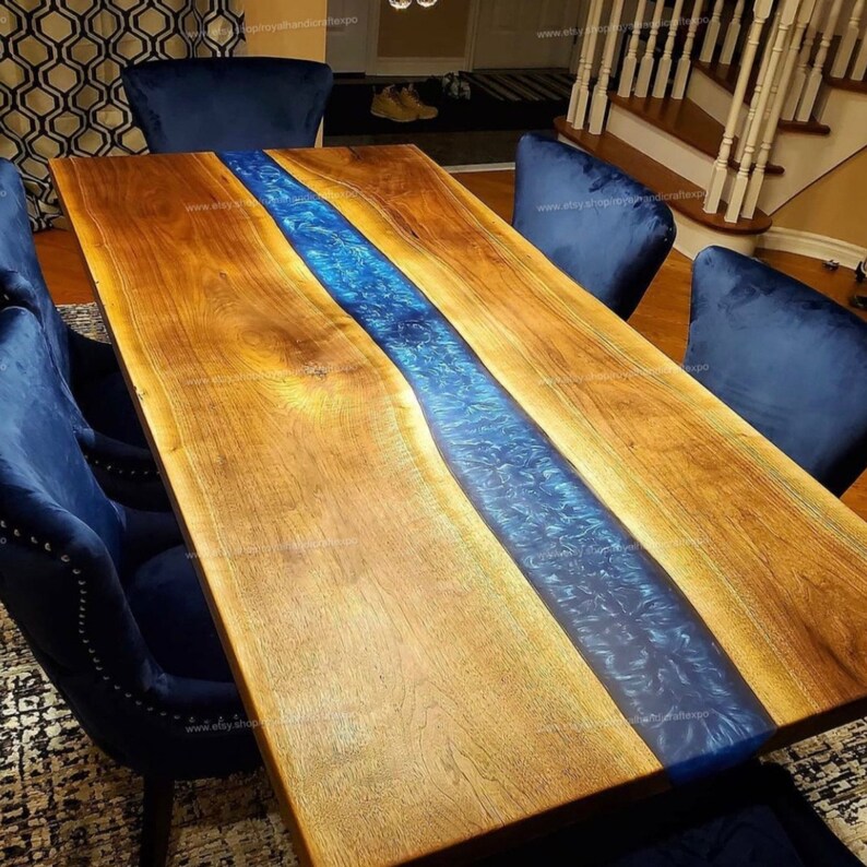May include: A large wooden dining table with a blue epoxy river running down the center. The table is surrounded by blue velvet chairs.