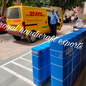 May include: Two large blue boxes with white tape and labels are being loaded into a yellow DHL delivery van. The boxes are stacked on top of each other. The van has the DHL logo and the words "Excellence Simple Deliveries" on the side.