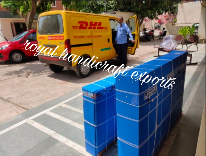 May include: Two large blue boxes with white tape and labels are being loaded into a yellow DHL delivery van. The boxes are stacked on top of each other. The van has the DHL logo and the words "Excellence Simple Deliveries" on the side.