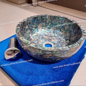 May include: A round, blue, green, and white mosaic sink with a chrome drain stopper. The sink is made of mother of pearl and is sitting on a blue velvet surface.