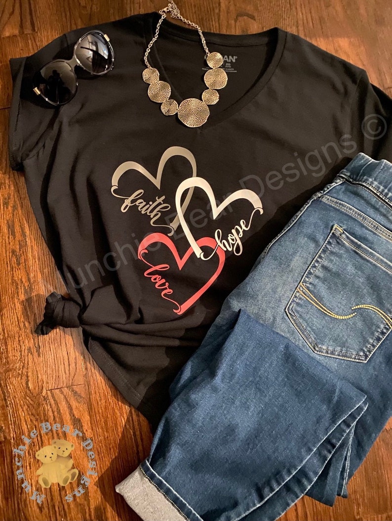 May include: Black t-shirt with a silver and pink heart design. The hearts have the words "faith", "love", and "hope" written on them.