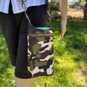May include: A camouflage print crossbody bag with a zipper closure. The bag has a black strap and a silver clasp.