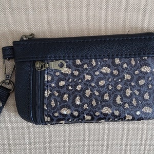 May include: A small black zippered pouch with a gold glitter leopard print fabric lining. The pouch has a black strap with a metal clip.
