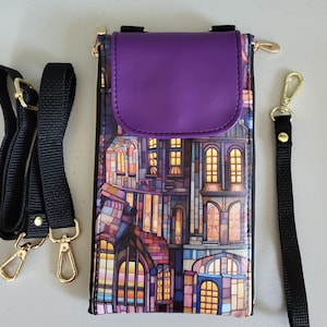 May include: A purple and multi-colored crossbody phone bag with a stained-glass building design. The bag has a purple flap, a black adjustable strap, and a black wrist strap. Gold-colored hardware is used for the zippers and clasps.