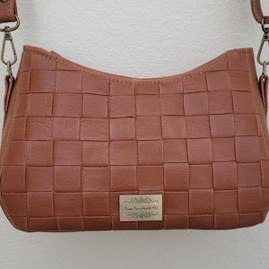 May include: A brown leather crossbody bag with a woven pattern. The bag has a small metal tag that says "Buya Handmade Hill".