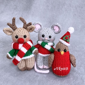 Puede incluir: Tres pequeños animales de peluche tejidos que incluyen un reno color canela con nariz roja y bufanda a rayas, un ratón gris con suéter rojo y bufanda verde y blanca, y un pájaro marrón con gorro rojo, pompón blanco y detalle de acebo.