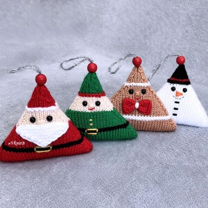 May include: Four triangular knitted ornaments featuring holiday characters: a red Santa with a white beard, a green elf, a tan gingerbread person with a red bow tie, and a white snowman with a black hat. Each has a red bead and silver hanging loop.