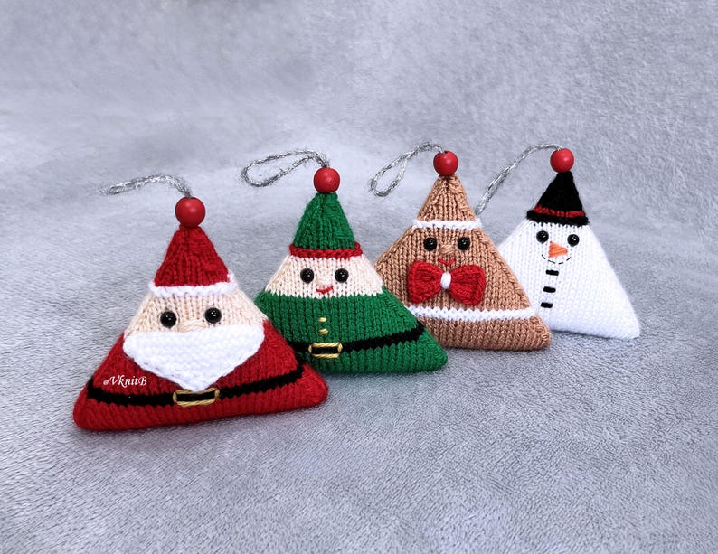 May include: Four triangular knitted ornaments featuring holiday characters: a red Santa with a white beard, a green elf, a tan gingerbread person with a red bow tie, and a white snowman with a black hat. Each has a red bead and silver hanging loop.