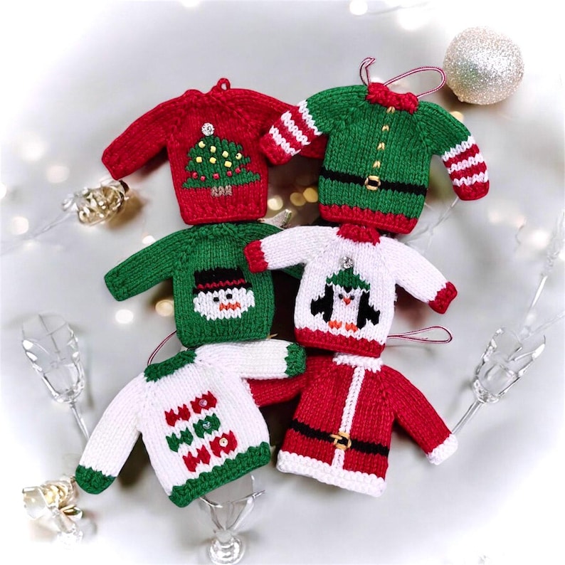 Collection of miniature knitted Christmas sweater ornaments in red, green, and white with festive designs including tree, snowman, and penguin.