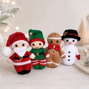 Puede incluir: Cuatro muñecos tejidos que incluyen a Santa Claus con traje rojo, un elfo con atuendo verde, una figura de pan de jengibre con pajarita roja y un muñeco de nieve blanco con sombrero negro, todos con detalles faciales bordados.