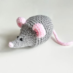May include: A grey knitted mouse with pink ears and a long tail. The mouse has black eyes and a pink nose.