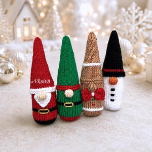 Puede incluir: Cuatro figuras de gnomos tejidas con diseños festivos. La primera es roja con barba y cinturón blancos. La segunda es verde con cinturón. La tercera es color canela con pajarita roja. La cuarta es blanca con gorro y nariz negros. El texto dice VknitB.