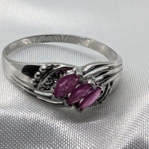 May include: A silver ring with a delicate design featuring a cluster of pink gemstones.