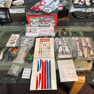 May include: A model kit of a racing boat with the text "BEACON PLUMBING" on the box. The kit includes various plastic parts, decals, paints, and instructions. The box shows images of the finished boat in red and white.