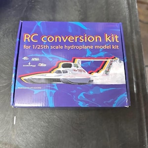 May include: A blue box with the text "RC conversion kit" for a 1/25th scale hydroplane model kit. The box features a graphic of a white and red hydroplane. The text "Model boat kit sold separately" is also visible.