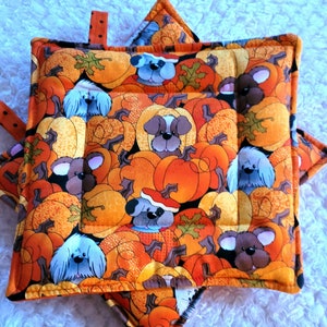 May include: Set of two orange and brown quilted pot holders with a pattern of dogs and pumpkins. The pot holders have a star shape and are made of fabric.