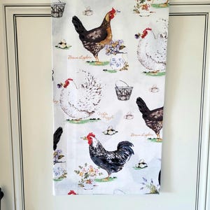 May include: A white kitchen towel with a repeating pattern of chickens and eggs. The chickens are brown, white, and black and white. The text "Brown Leghorn", "White Frizzle", and "White Frizzle" is printed on the towel.