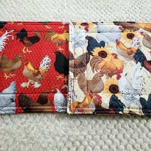May include: Two fabric placemats with chicken and sunflower patterns. One placemat has a red background with a chicken wire design. The other has a cream background with sunflowers. The placemats are rectangular and likely for kitchen use.