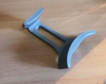 Op de afbeelding: Een grijze 3D-geprinte telefoonstandaard van plastic met een gebogen basis en een gleuf om een telefoon vast te houden.