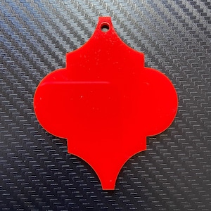 May include: A bright red, decorative ornament shaped like a quatrefoil, with a small hole at the top for hanging.