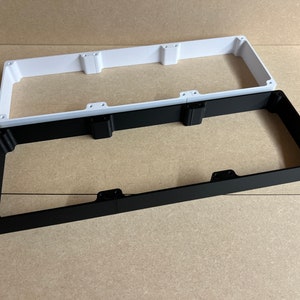 May include: Two rectangular frames, one white and one black, are stacked on top of each other. The frames are made of a hard plastic material and have a smooth finish.
