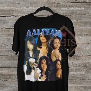 May include: Black t-shirt featuring a collage of images of singer Aaliyah. The images are in a blue and white colour scheme. The text "Aaliyah" is printed in blue and white on the shirt.