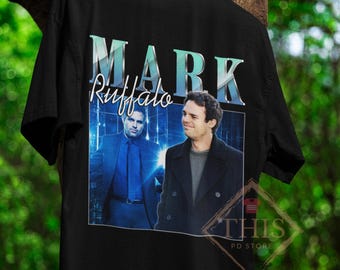 May include: Black t-shirt with a graphic print of Mark Ruffalo in a blue suit and a black coat. The text "MARK Ruffalo" is printed in blue and white letters on the shirt.