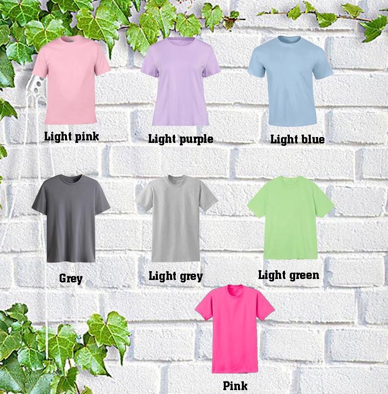May include: Seven different color t-shirts displayed on a white brick wall. The colors are light pink, light purple, light blue, grey, light grey, light green, and pink.