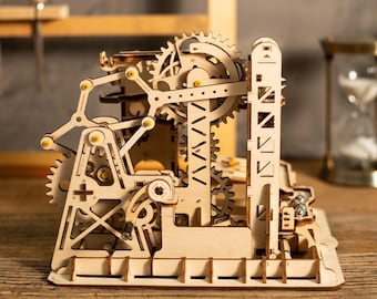 May include: A wooden mechanical model with intricate gears, levers, and a tower-like structure. The model is made of light-colored wood and features a complex design with multiple interlocking parts. The gears are visible and appear to be functional.