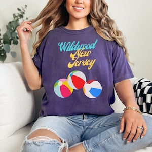 May include: Purple t-shirt with the text "Wildwood New Jersey" in a retro font and three beach ball graphics.