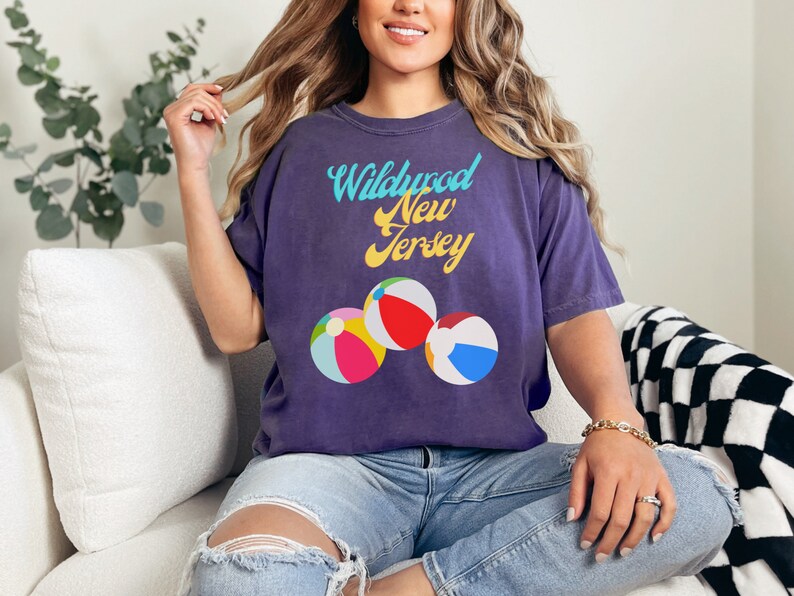 May include: Purple t-shirt with the text "Wildwood New Jersey" in a retro font and three beach ball graphics.
