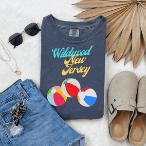 May include: A dark blue t-shirt with the text "Wildwood New Jersey" in yellow and blue lettering. The shirt features three colorful beach balls.